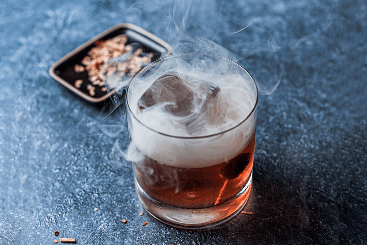 Potente cóctel elaborado a base de bourbon, maraschino y refresco de jengibre, destaca su sirope ahumado de Polot TATEL.