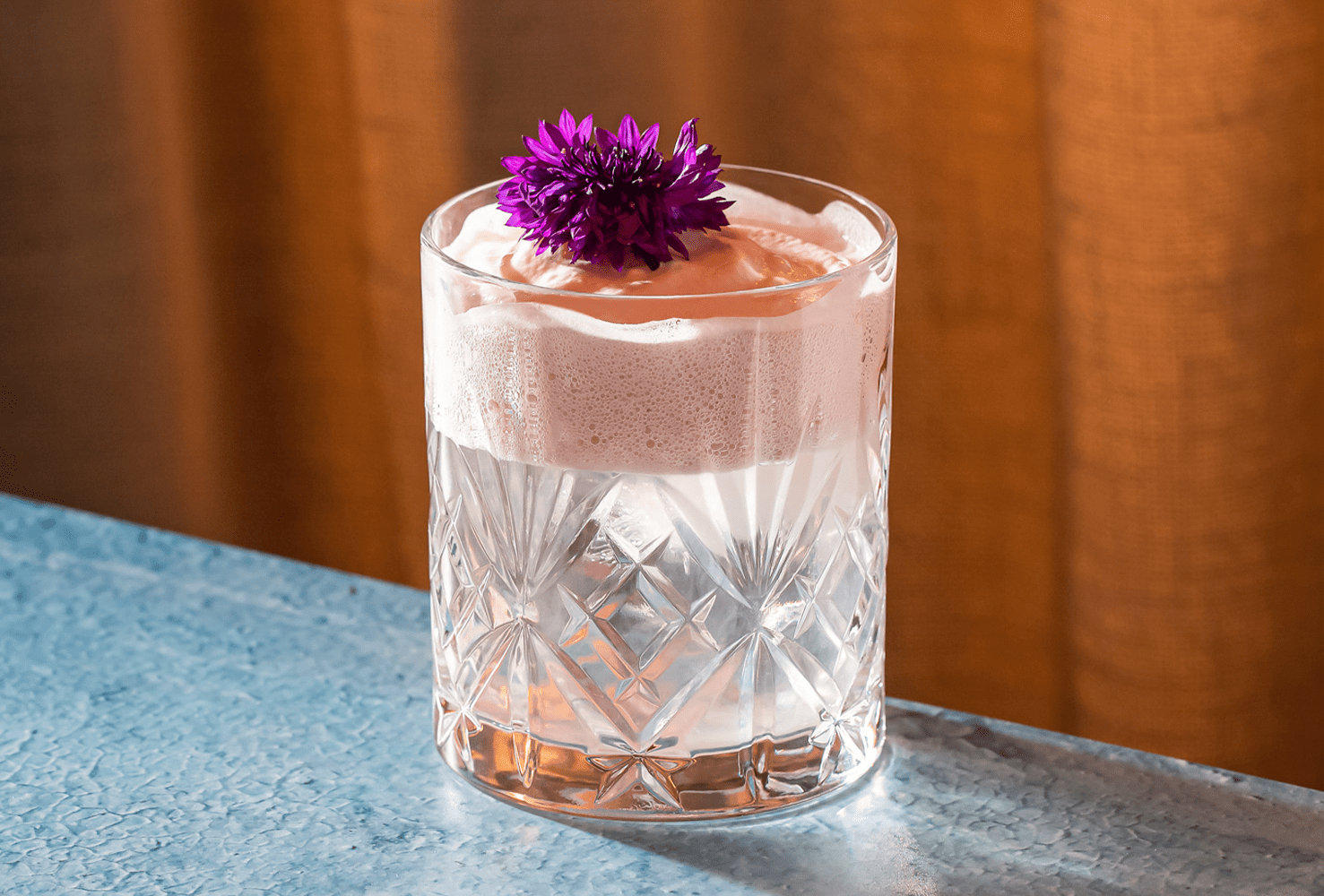 Coctel con espumoso servido en un elegante vaso de cristal adornado con una flor violeta.